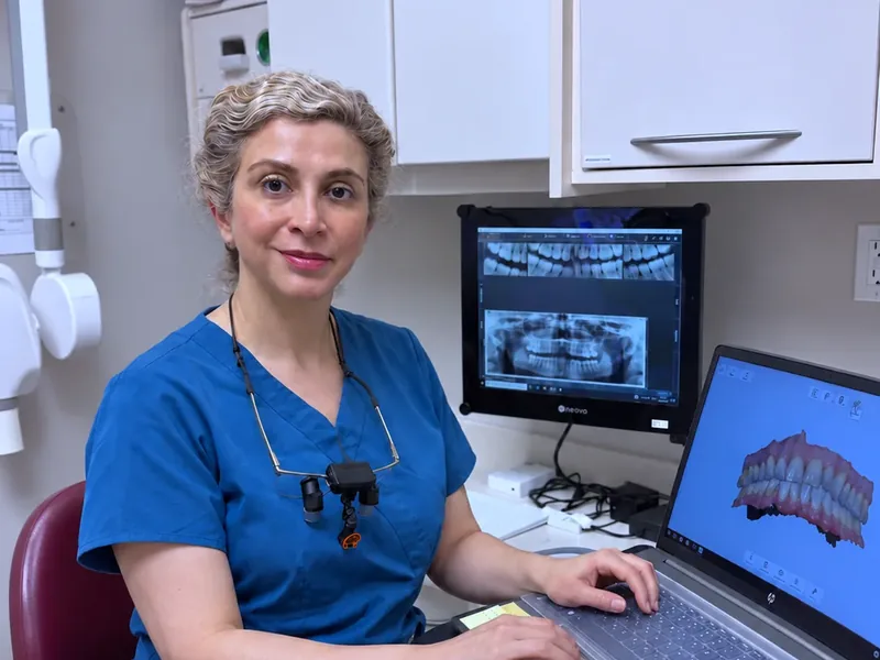 Dr. Okhravi at her desk beside a laptop showing a 3D scan of a patient’s teeth